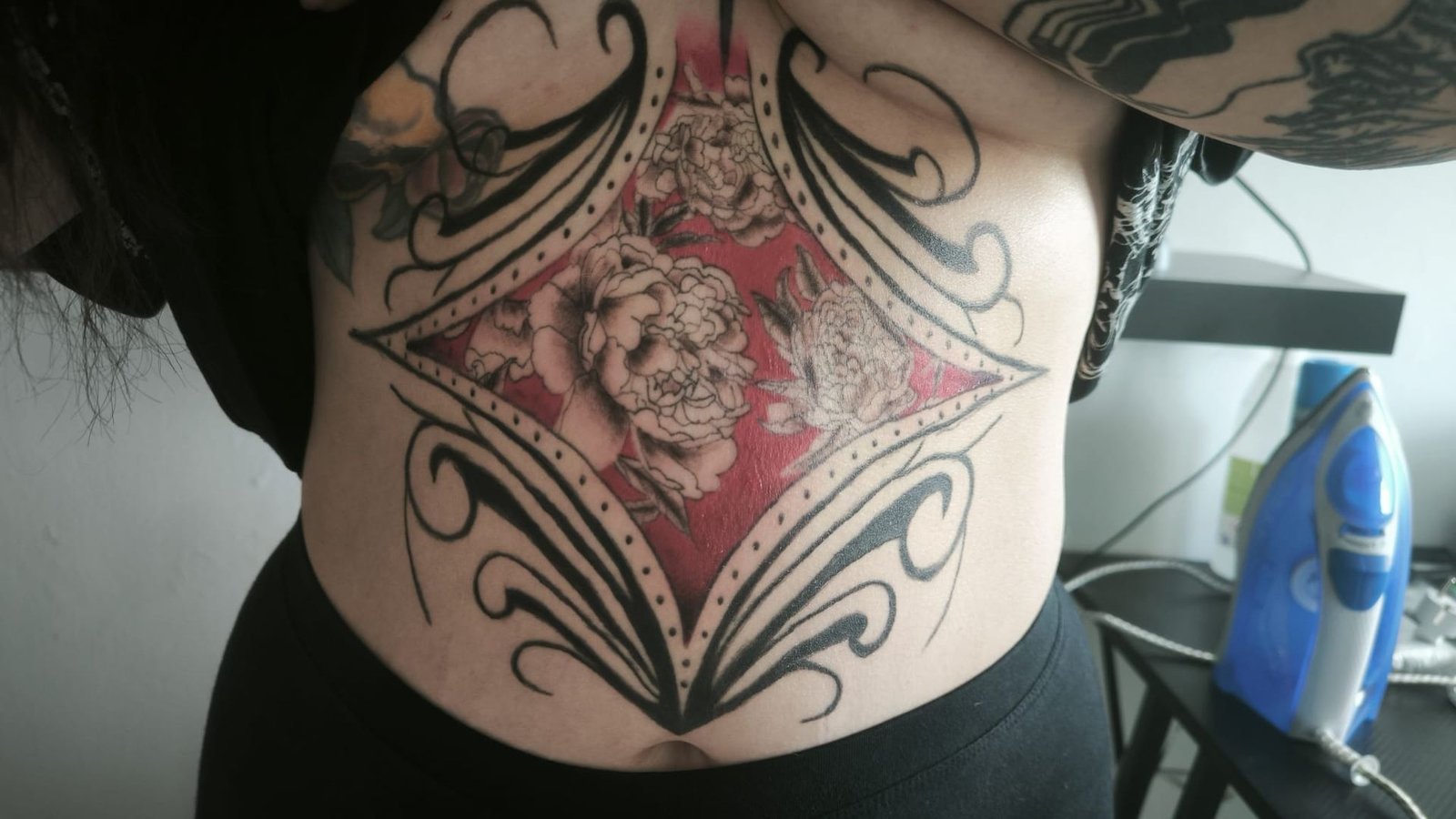 Torso con un gran tatuaje de una rosa enmarcado por espirales ornamentales negras y detalles rojos.