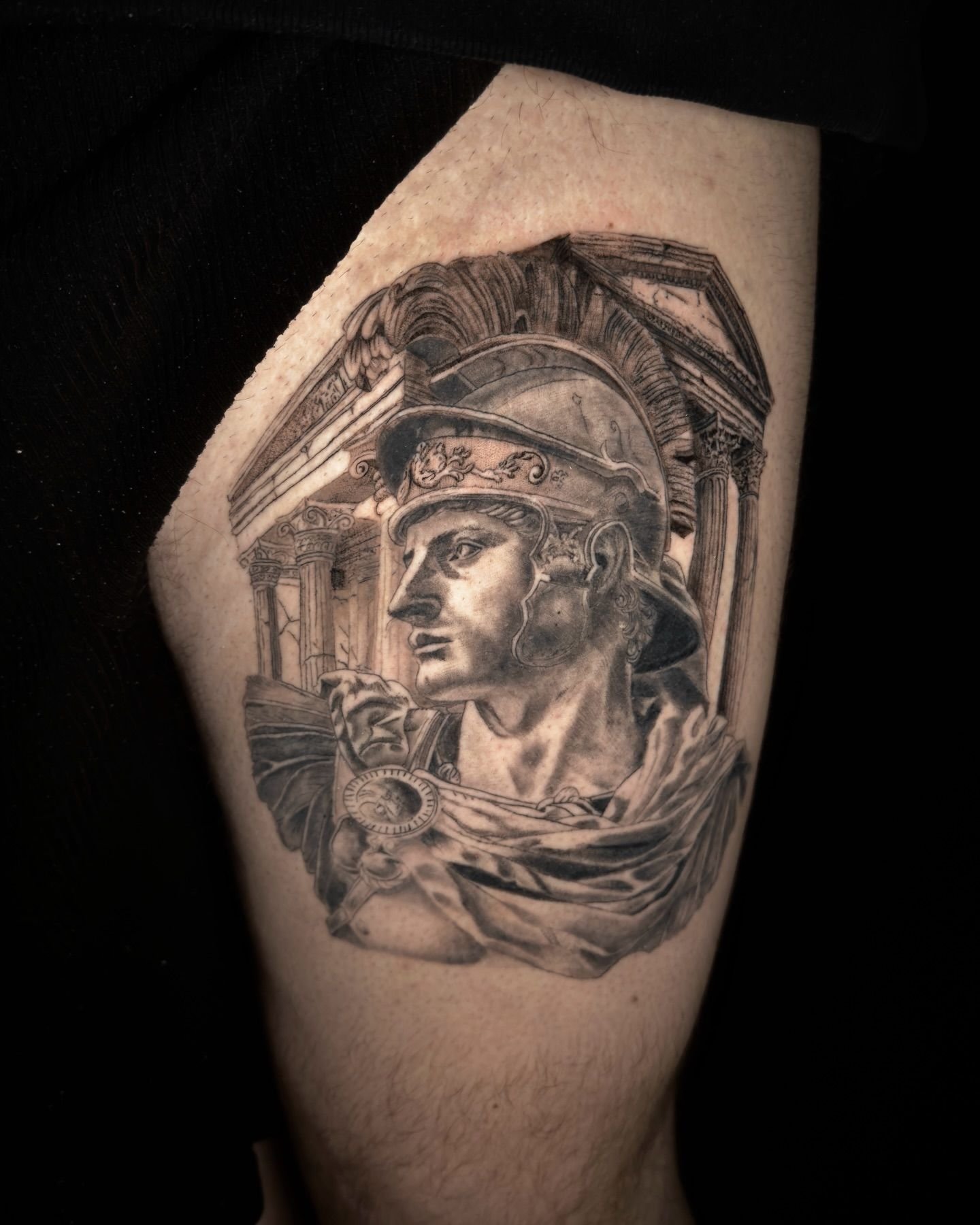 Tatuaje en blanco y negro de un casco y rostro de guerrero clásico en la parte superior del brazo.
