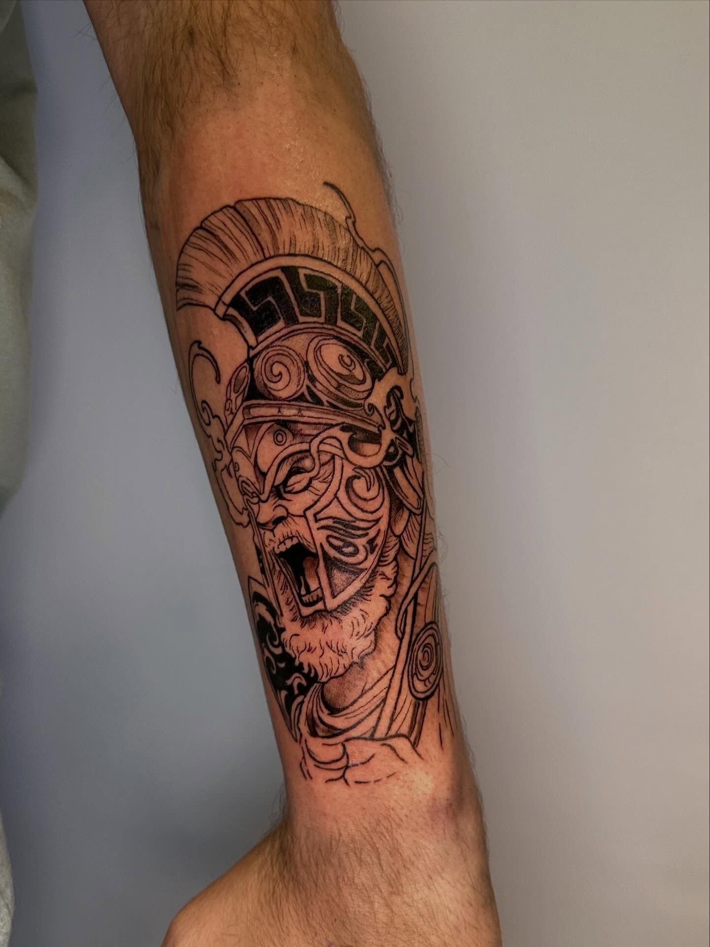Tatuaje en el antebrazo de un rostro o máscara estilizada en tinta negra.