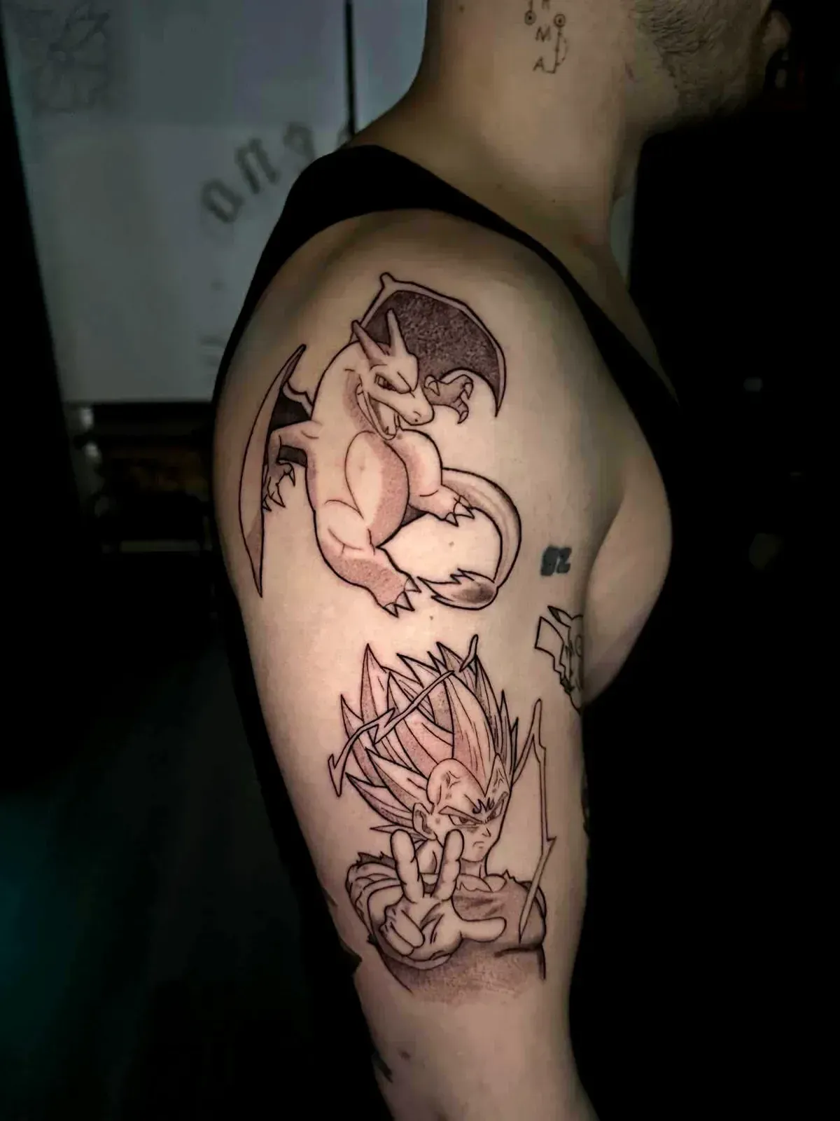 Dos tatuajes de personajes de dibujos animados en blanco y negro en la parte superior del brazo, con un pequeño contorno en forma de diamante cerca.